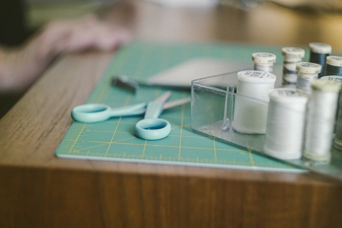 Turquoise scissors and white thread rest on a cutting mat.